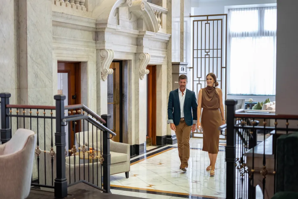 Elegant lobby with marble floors, ornate design, couple walking to elevators, and stylish seating.